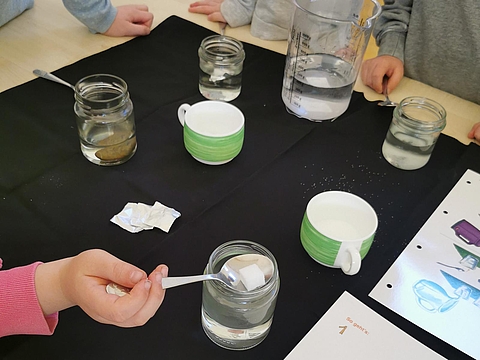 Kinder lösen Zucker und andere Lebensmittel in Wassergläsern auf. 