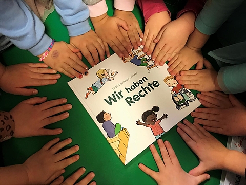 Kinderhände auf dem Buch "Wir haben Rechte"